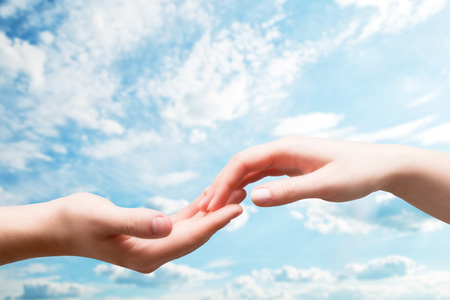 Man and woman hands touch in gentle, soft way on blue sunny sky